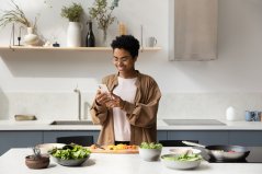 Vrouw in keuken, kijkend op telefoon Vrouw in keuken, kijkend op telefoon